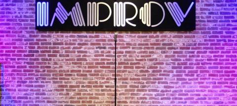 stage with brick wall behind it with a sign that reads improv, a mic stand is centered on the stage