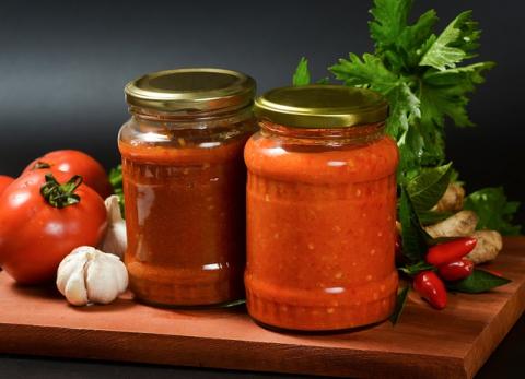 Two jars of chili sauce surrounded by various vegetables: garlic, tomatoes, chili peppers