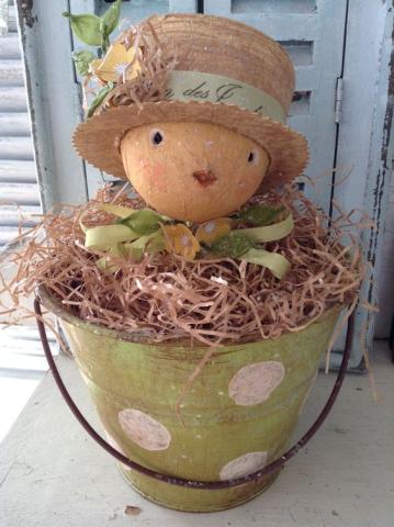 A paper chick in a hat in a bucket filled with nesting 