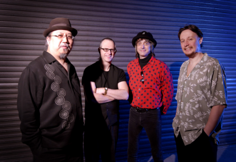 Portrait of four men from the waist up, standing in a row, dressed hip, smiling at the camera