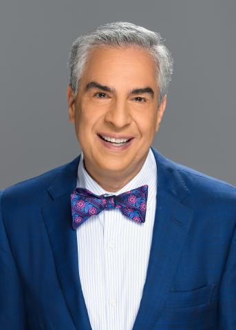 Headshot photograph of a smiling man with grey hair, wearing a suit jacket and colorful bow tie