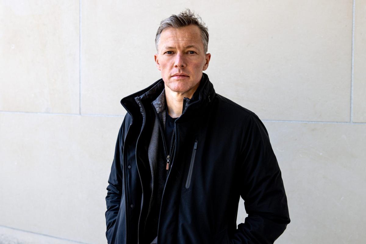 Portrait of a serious looking man with grey hair and dark clothes staring straight at the camera